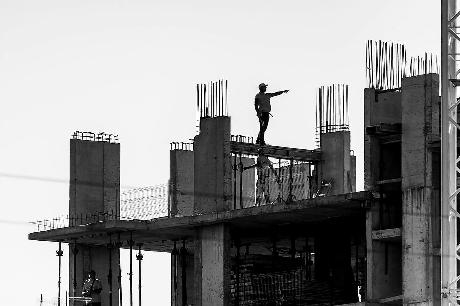 Free Silhouette of construction workers on a building site with one pointing towards the distance. Stock Photo