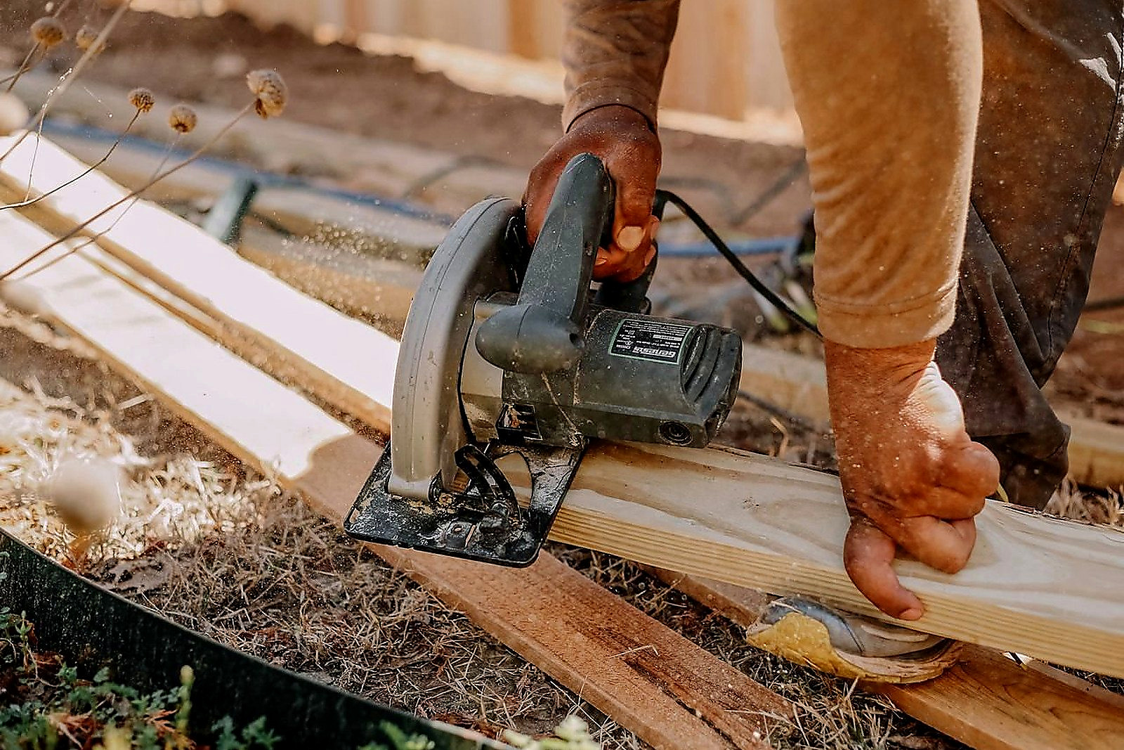 Free Carpenter operating a circular saw on wooden planks outside, showcasing woodworking skills. Stock Photo